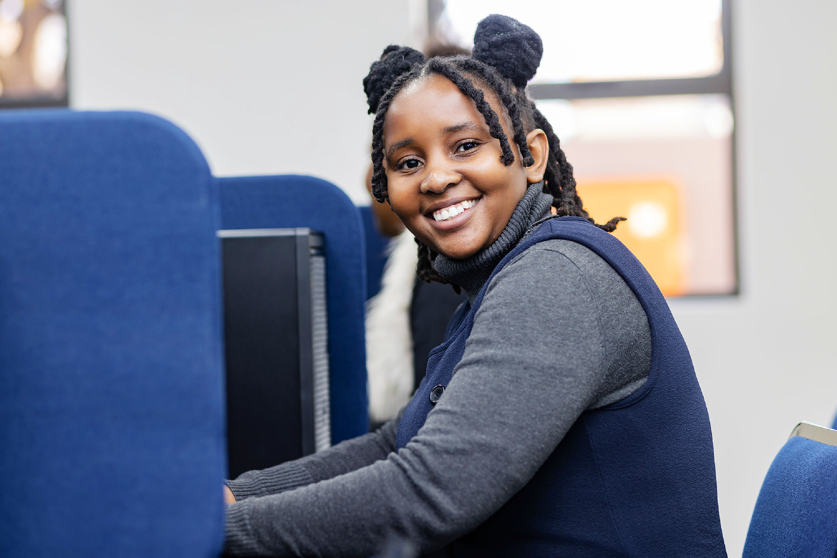 A picture of an excited lady sitting in front of a computer in class at Eduvos.